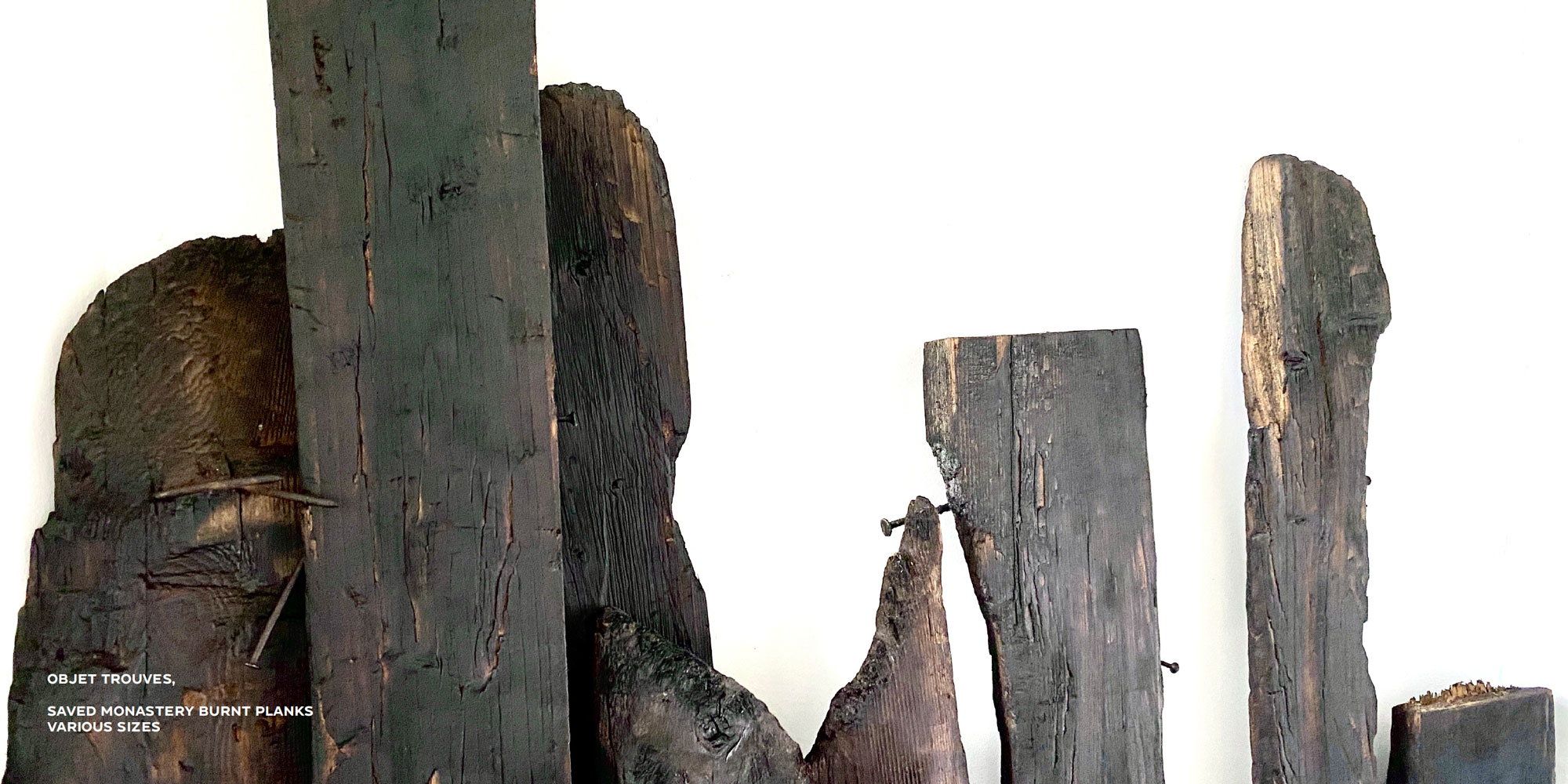 A series of burnt wooden floor boards with nails sticking out from them. The wooden planks are lined up against a white background.